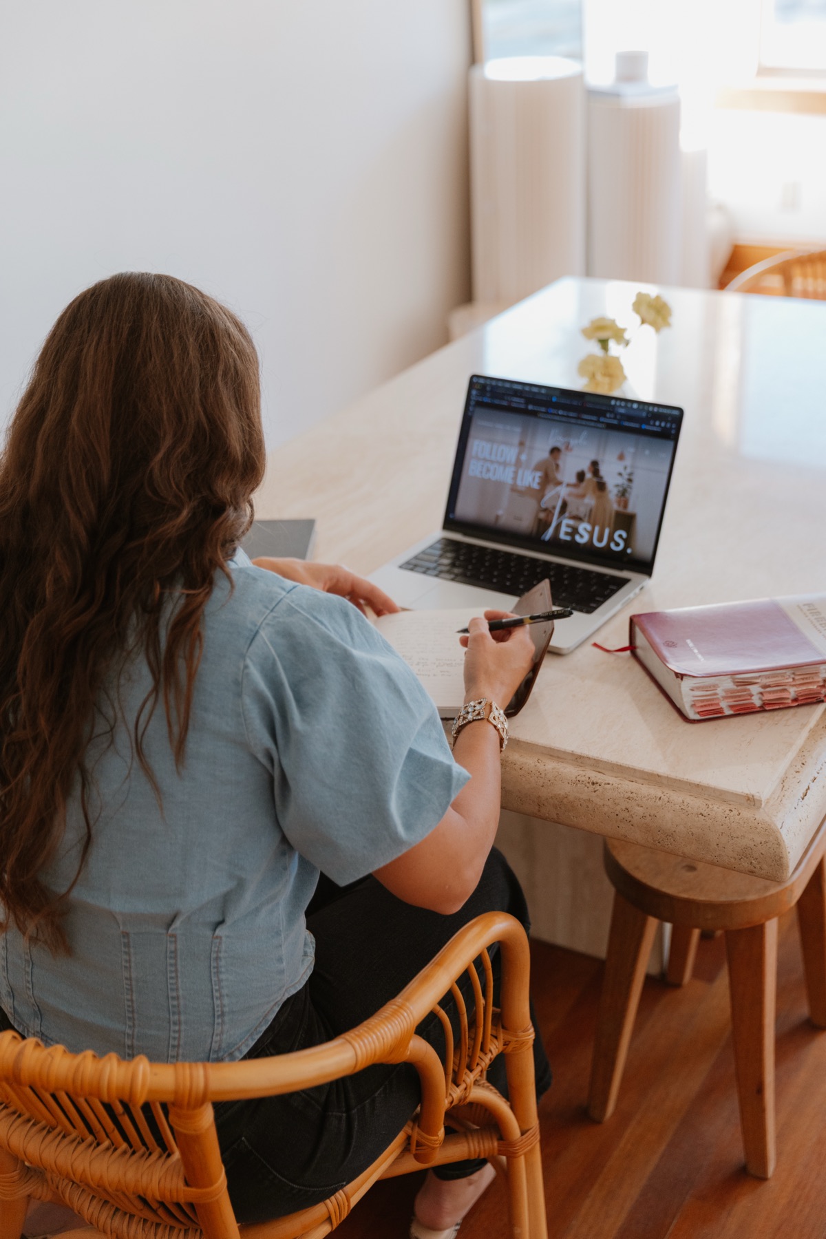A woman at a sunlit table with her Bible and a laptop open to a study about Jesus